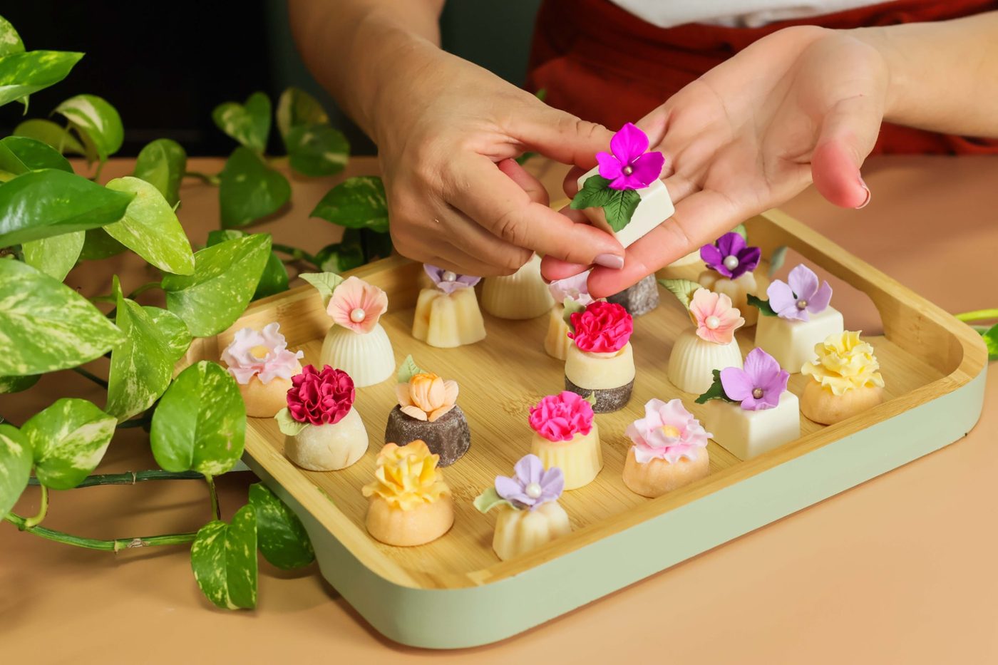 Mãos finalizando bandeja de doces finos com flores de açúcar coloridas